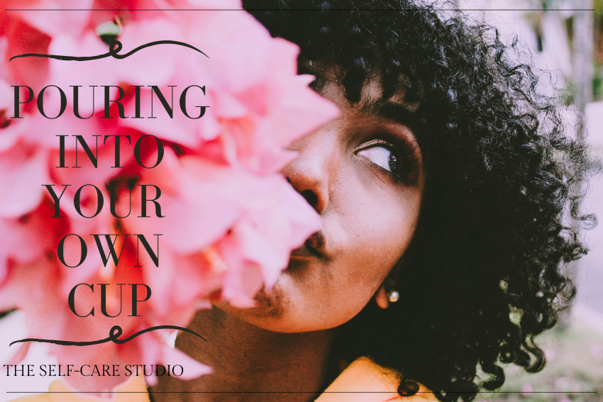 black woman with curly hair holding pink flowers partially in front of her face